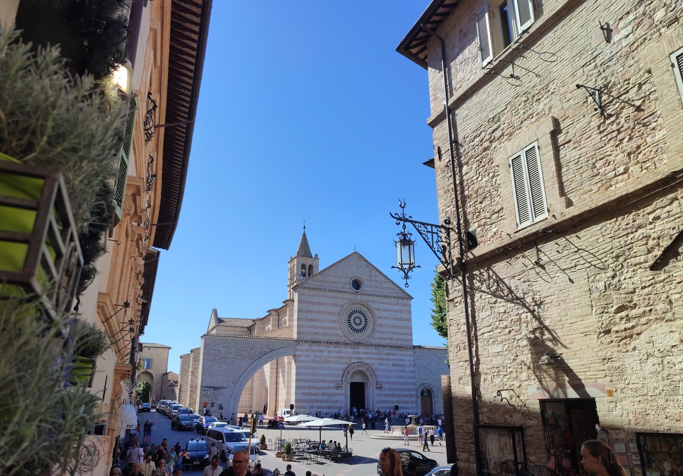 The striped pink and white facade of the Basilica di Santa Chiara in Assisi, seen from a side street