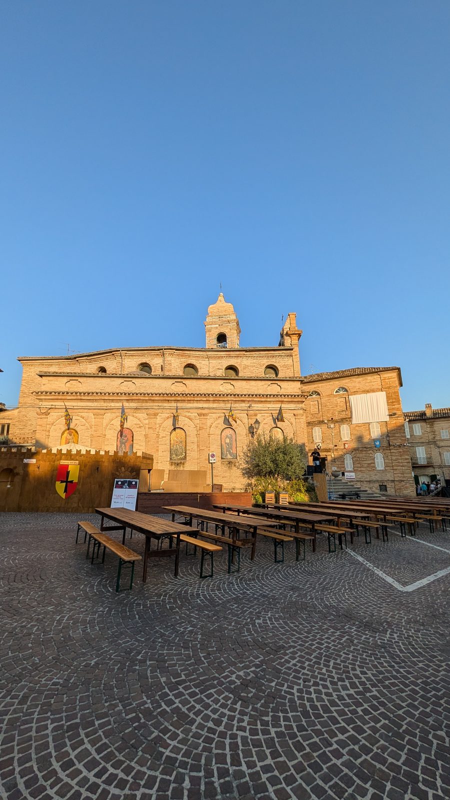 Taverna dell'Oca sign and long wooden tables in front of the church of San Giovanni Battista, Grottazzolina