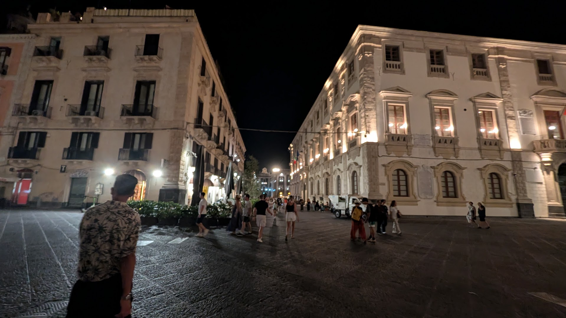 A street near Catania's Piazza dell'Università at night, with Baroque facades and evening crowds