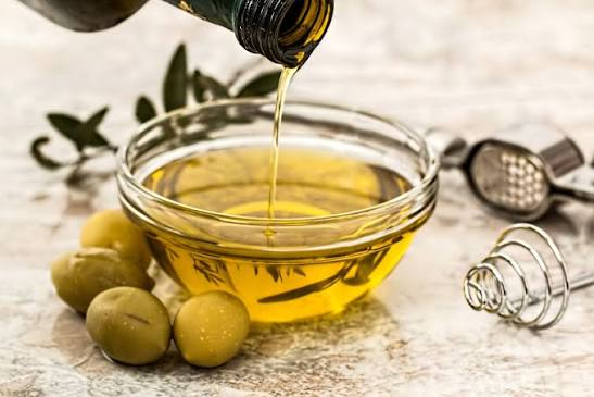 Extra virgin olive oil pouring into a bowl next to fresh green olives