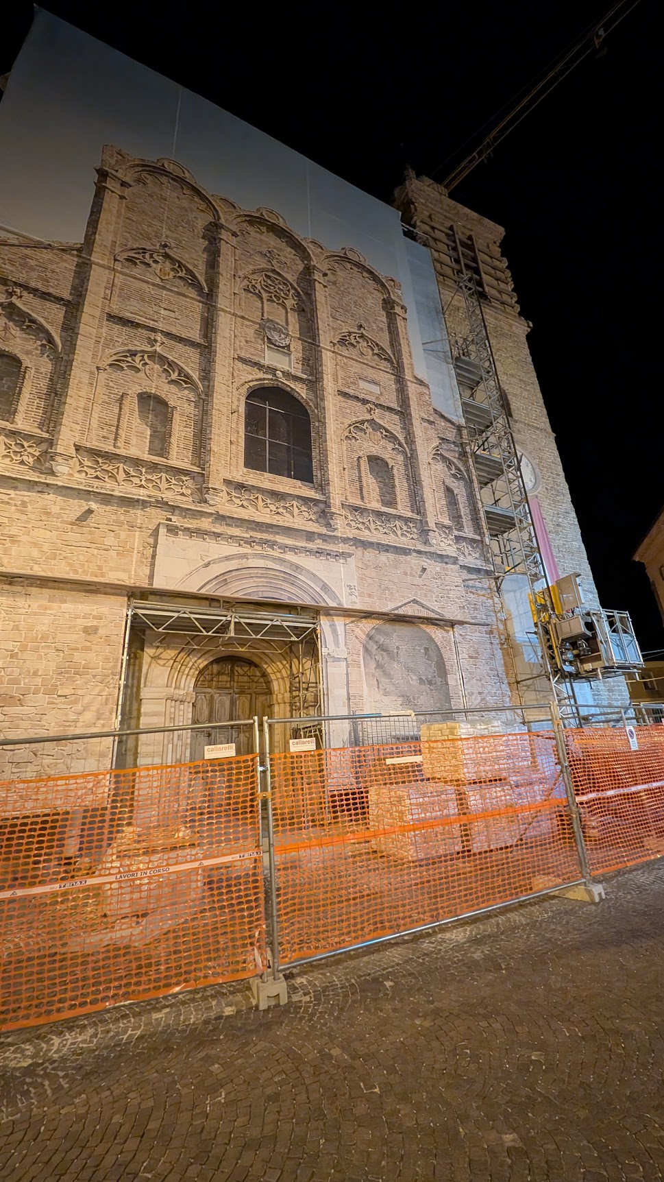 A church facade in the Marche wrapped in protective scaffolding during ongoing seismic reconstruction, photographed at night
