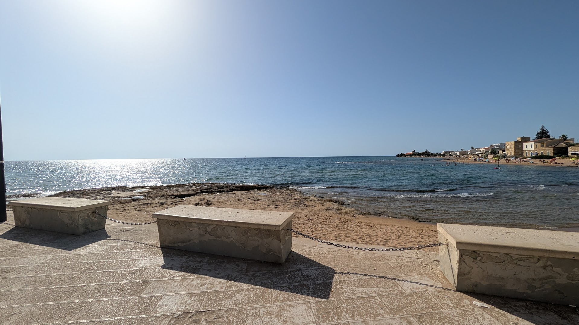 Stone benches along the seafront promenade at Punta Secca, Sicily, overlooking the beach