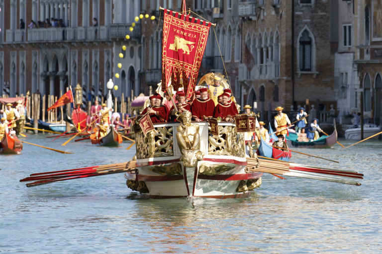 Costumed rowers aboard a ceremonial Venetian boat flying a Venezia banner during the Regata Storica historical procession