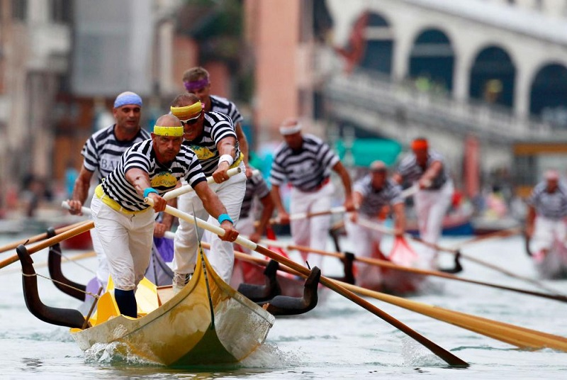 Rowers racing standing up in the voga alla veneta style during the Regata Storica near the Rialto Bridge