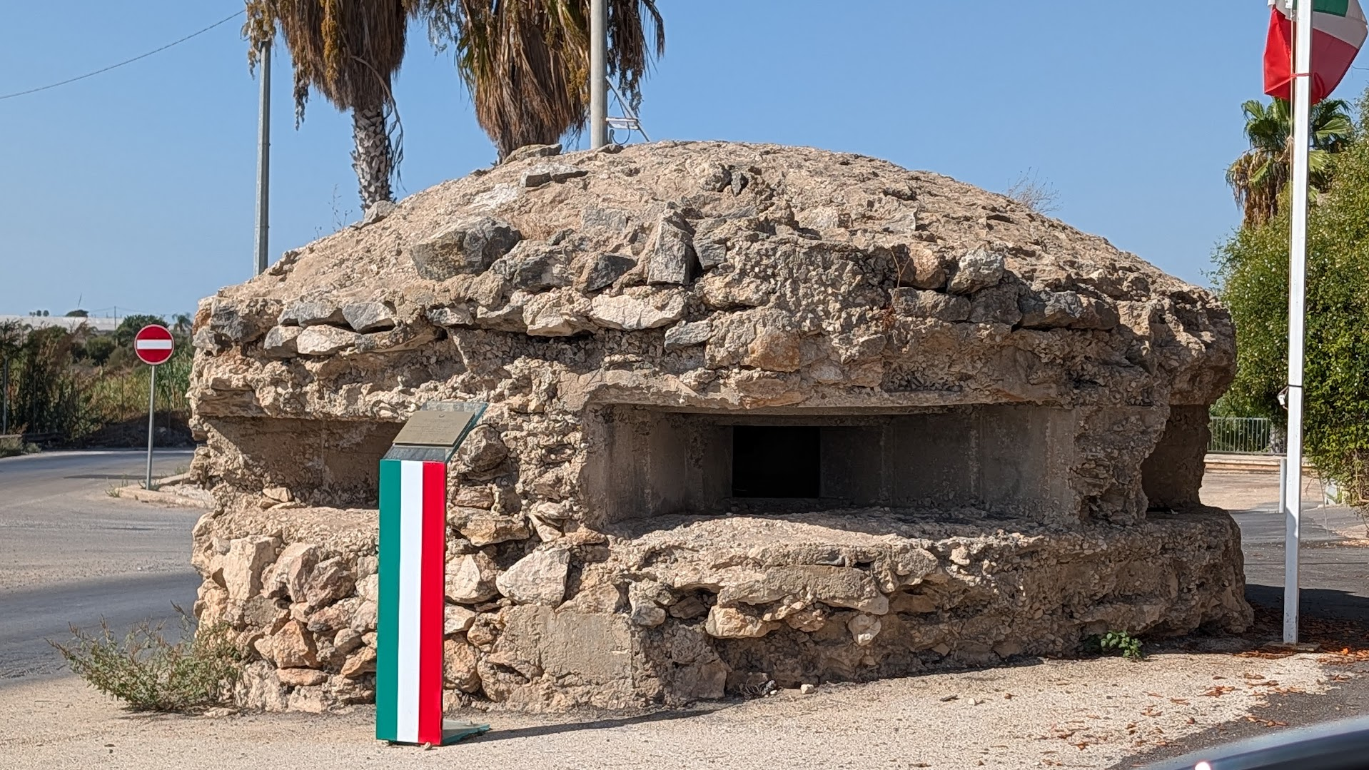 Reinforced concrete WWII coastal bunker at Santa Croce Camerina, Sicily, camouflaged with rough stone and marked with an Italian flag