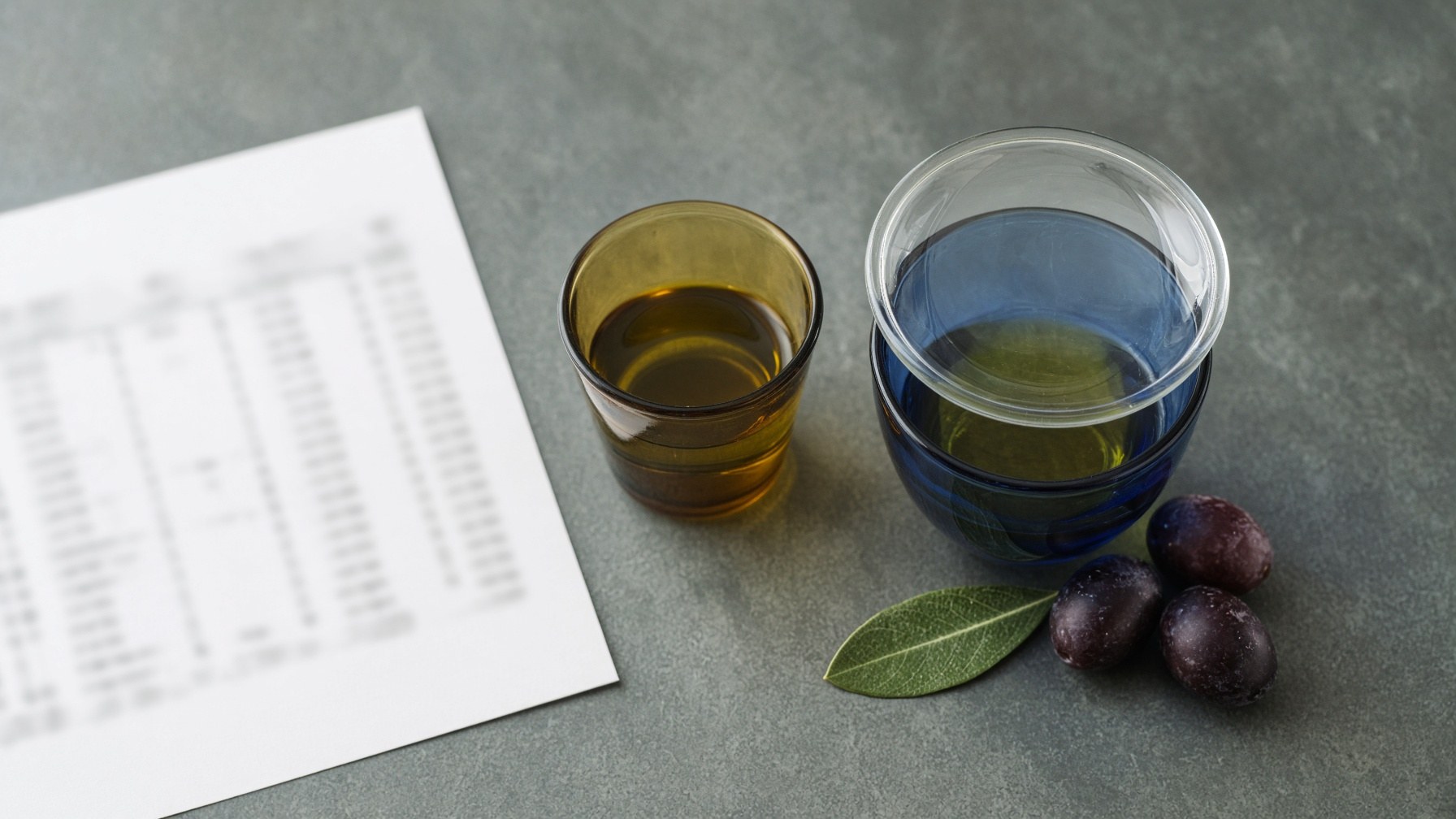 Analysis report and a blue sensory tasting glass of olive oil on a laboratory bench, illustrating what extra virgin olive oil means under EU law.